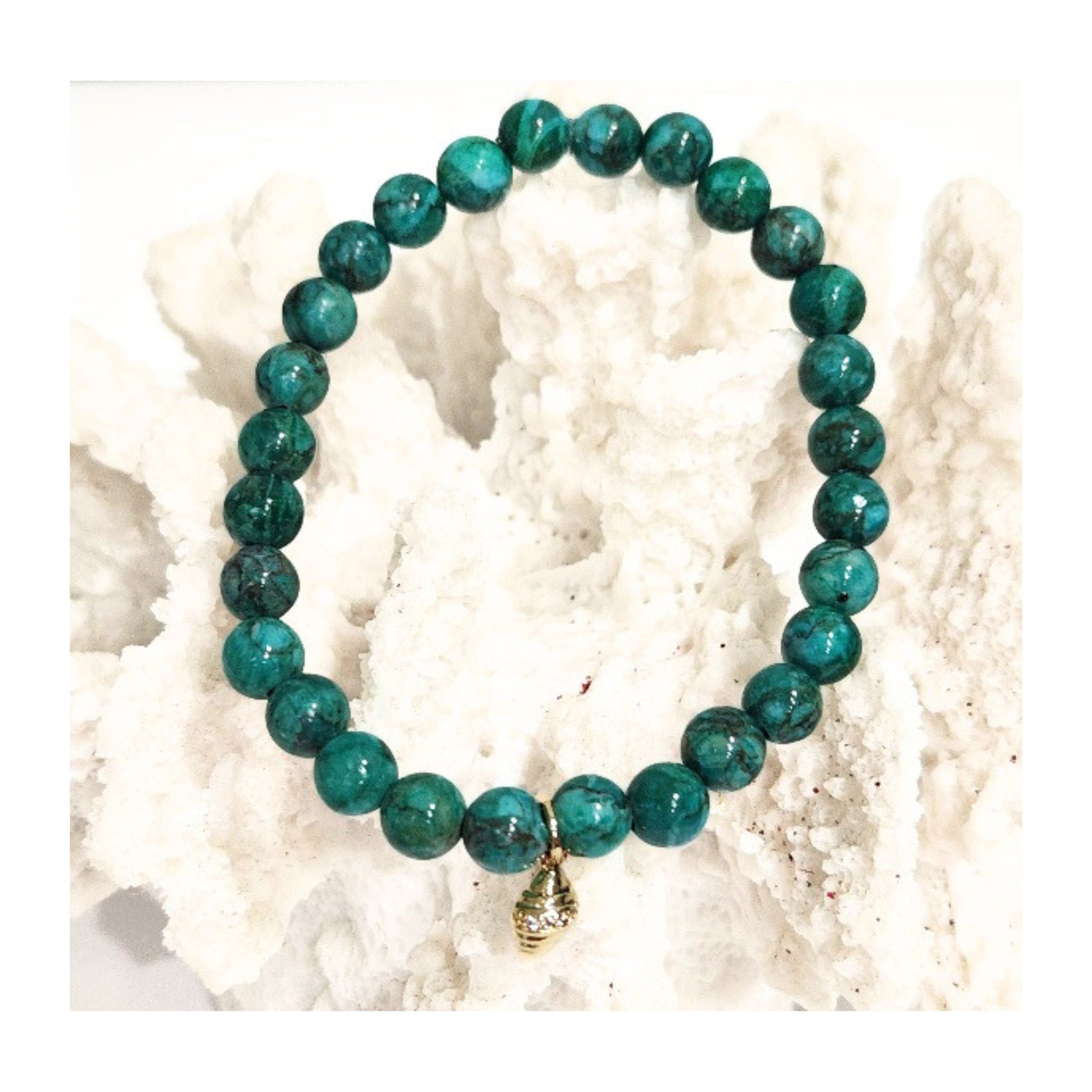 A full view of the African Turquoise stretch bracelet with a golden conch shell charm styled on a white textured reef decor piece for a coastal aesthetic by Coastline Boutique