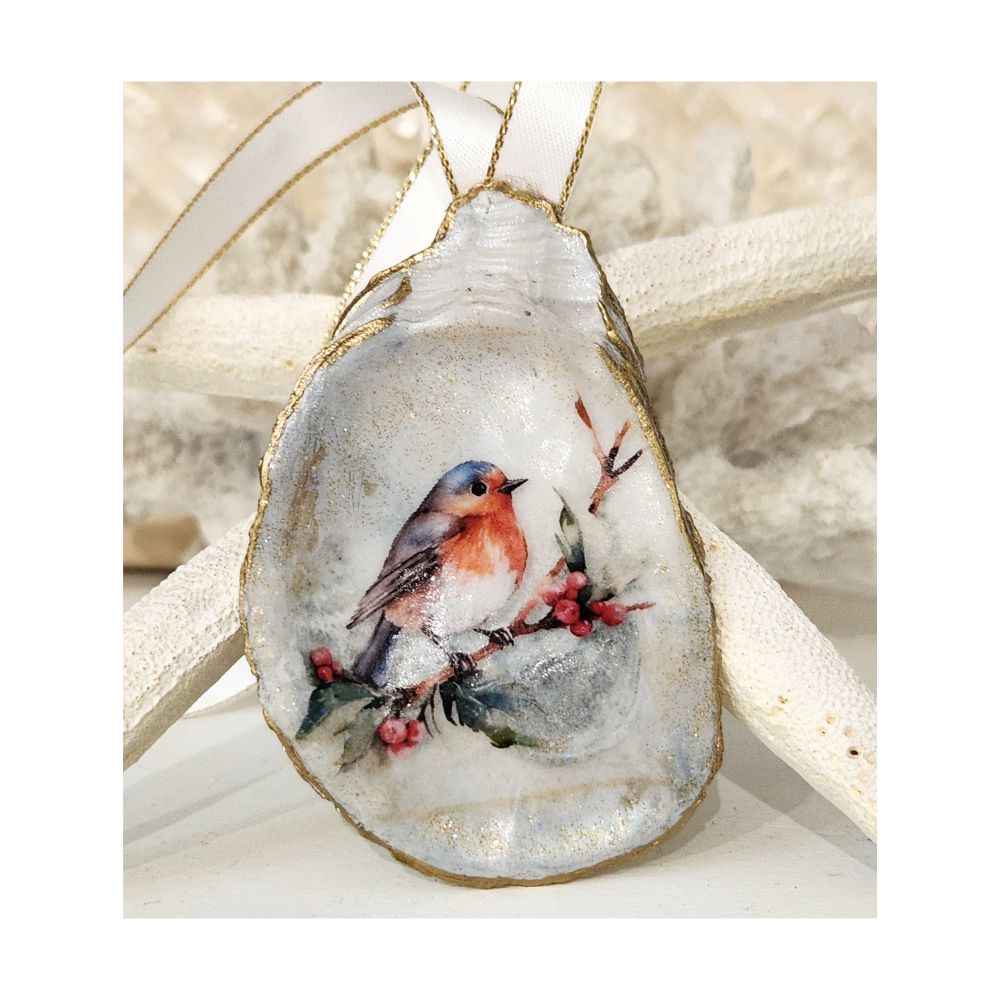 A handcrafted gilded oyster shell ornament featuring a decoupaged barn swallow perched on a twig with red berries and small leaves. The inside of the shell is finished with a delicate touch of sparkle, complete with a white and gold satin ribbon hanger against a starfish