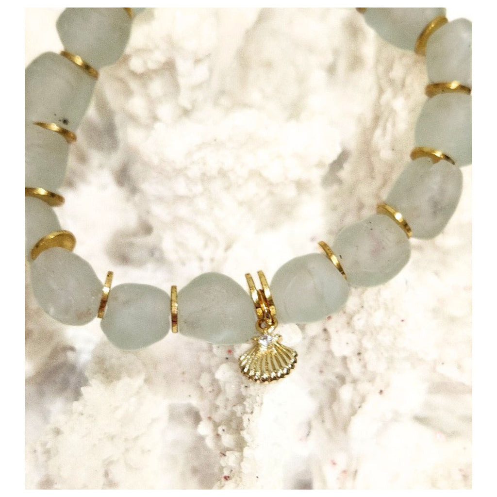 Close up detail of 9mm aqua recycled glass beads gold plated spacers and the tiny cz star shell charm displayed on a textured white coastal reef. 