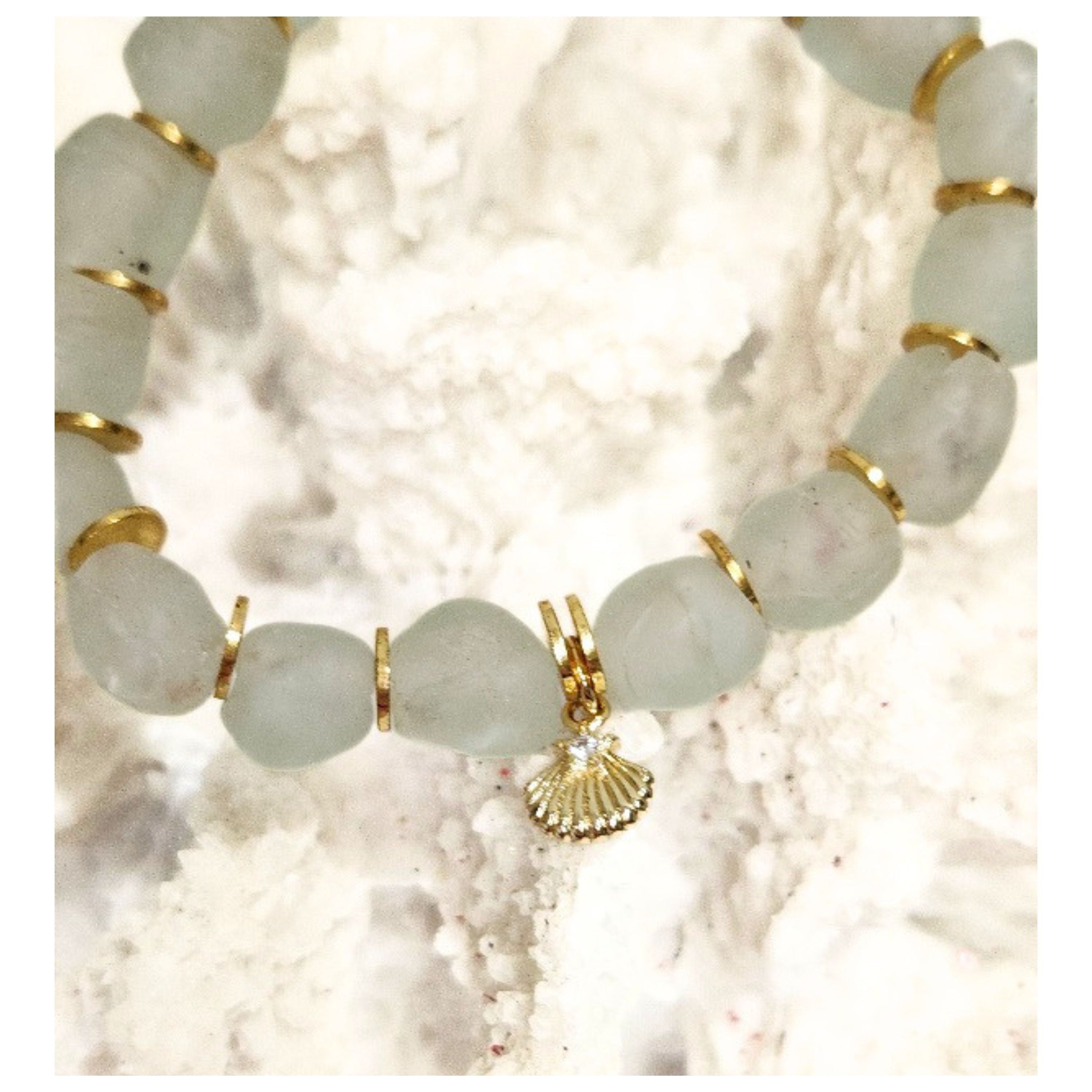 Close up detail of 9mm aqua recycled glass beads gold plated spacers and the tiny cz star shell charm displayed on a textured white coastal reef. 