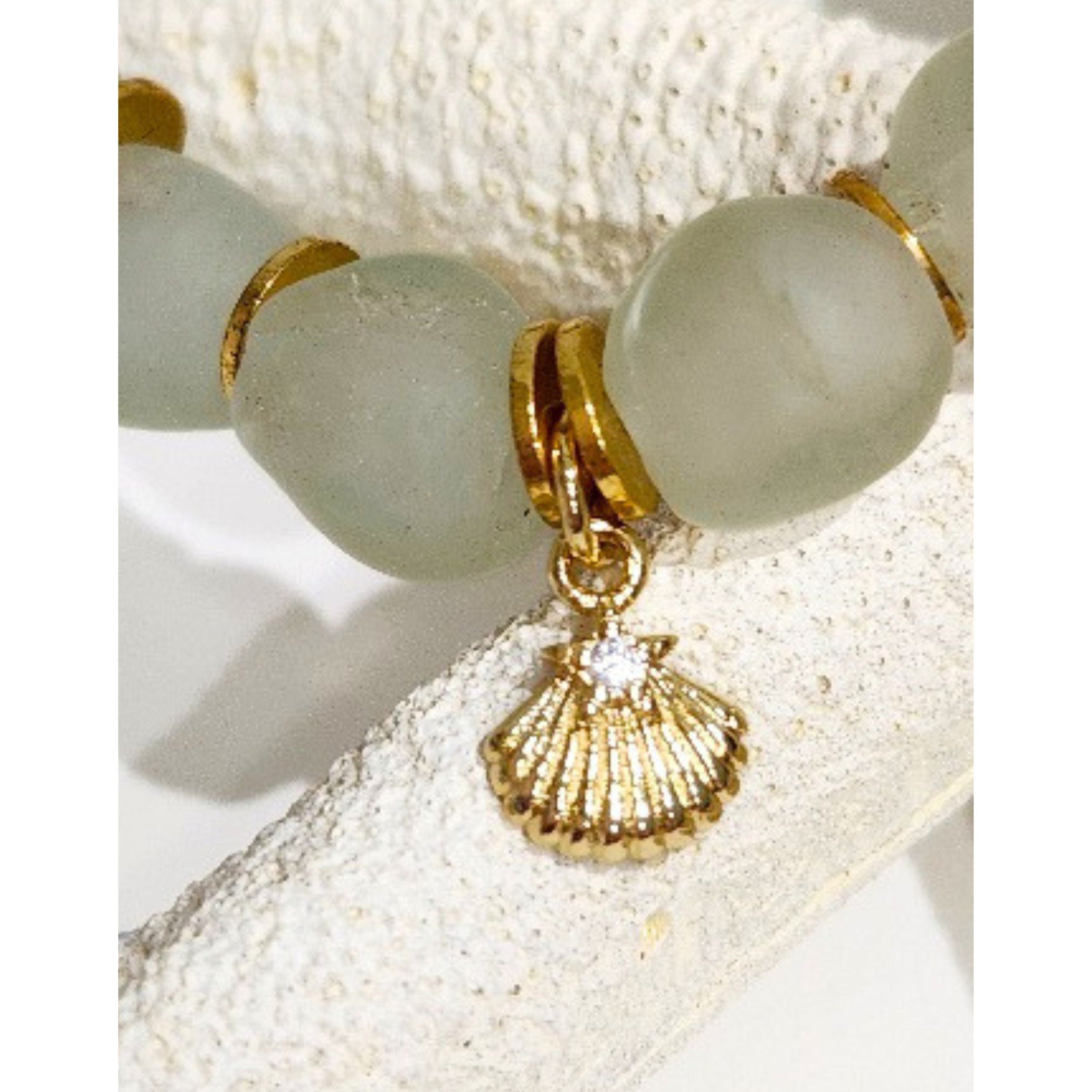 Macro close up of the Star Kissed Shell pendant highlighting the tiny sparkling CZ star and gold plated detail with a soft focus view of the aqua recycled glass beads on a white starfish background