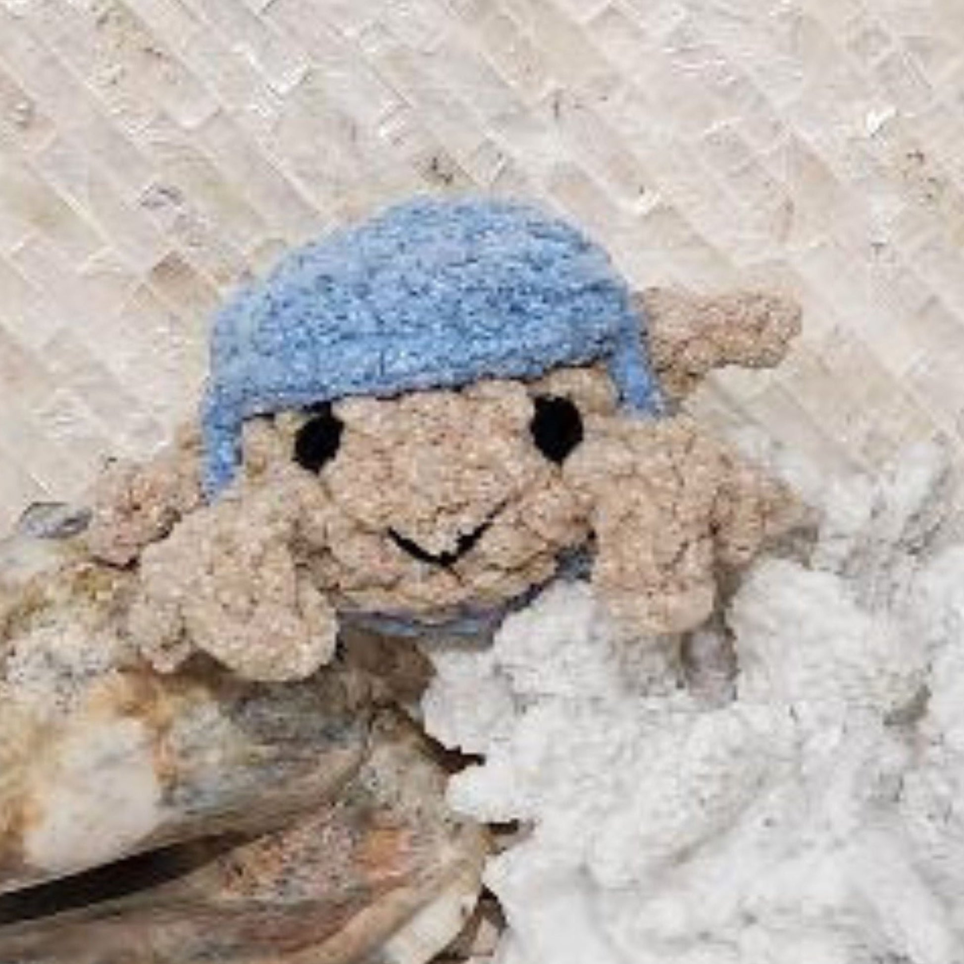 Close up face view of a handmade sandy crab featuring hand embroidered eyes and a friendly stitched smile framed by a vibrant blue crocheted hat