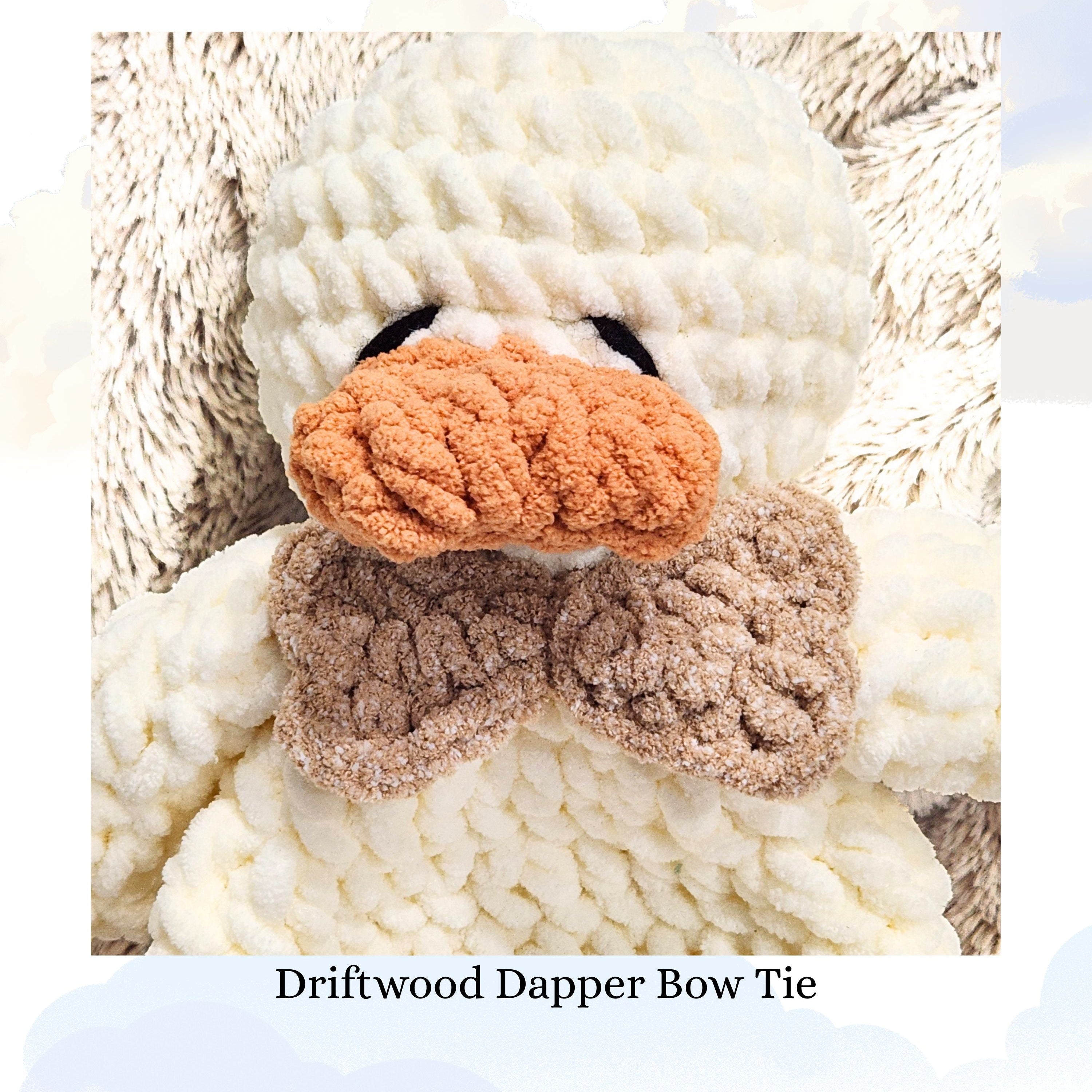 Close up detail of a Ducky Dreams crochet duck featuring a dapper driftwood brown bow tie.  The photo highlights the handmade crochet texture and neutral tones, with a soft focus background of a plush blanket and whimsical clouds