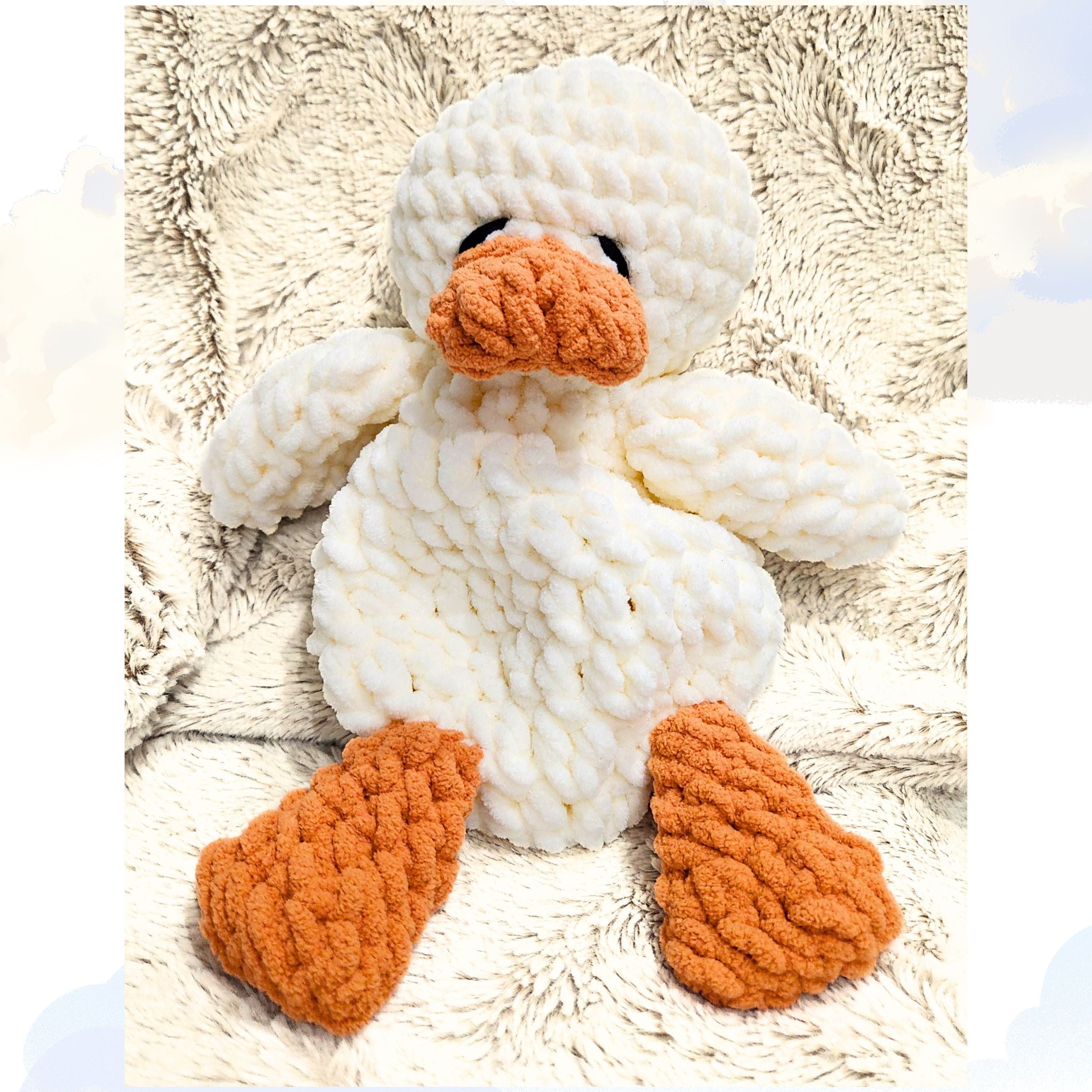 The classic Ducky Dreams vanilla cream crochet duck snuggler in a full body view. The plush duck is nestled on a soft blanket against a whimsical background of distant clouds, showcasing its simple, elegant design and safety first embroidered eyes