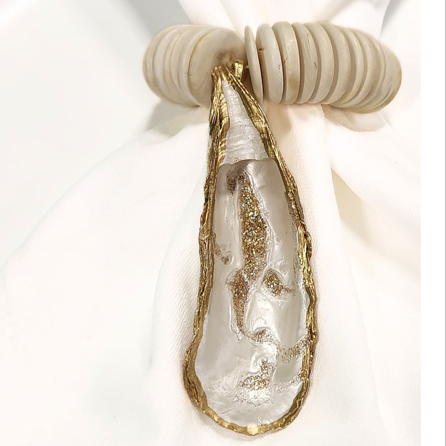 Hand-painted, gilded oyster shell napkin ring featuring smooth ivory coconut shell beads on a white linen napkin