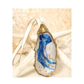 A handcrafted gilded oyster shell ornament featuring a nautical blue jellyfish design with flowing tentacles and gold sparkle accents. The shell is trimmed in brilliant gold leaf and finished with an ivory satin ribbon with gold trim, beautifully staged on a background of a natural starfish and white coral.