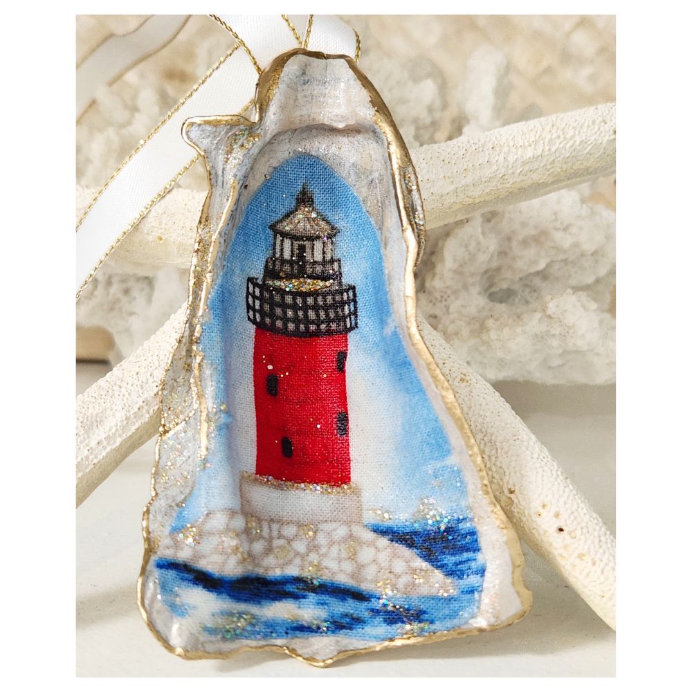 Handcrafted gilded oyster shell ornament featuring a classic red lighthouse on a nautical blue background, finished with an elegant white ribbon and hand-painted gold leaf trim.