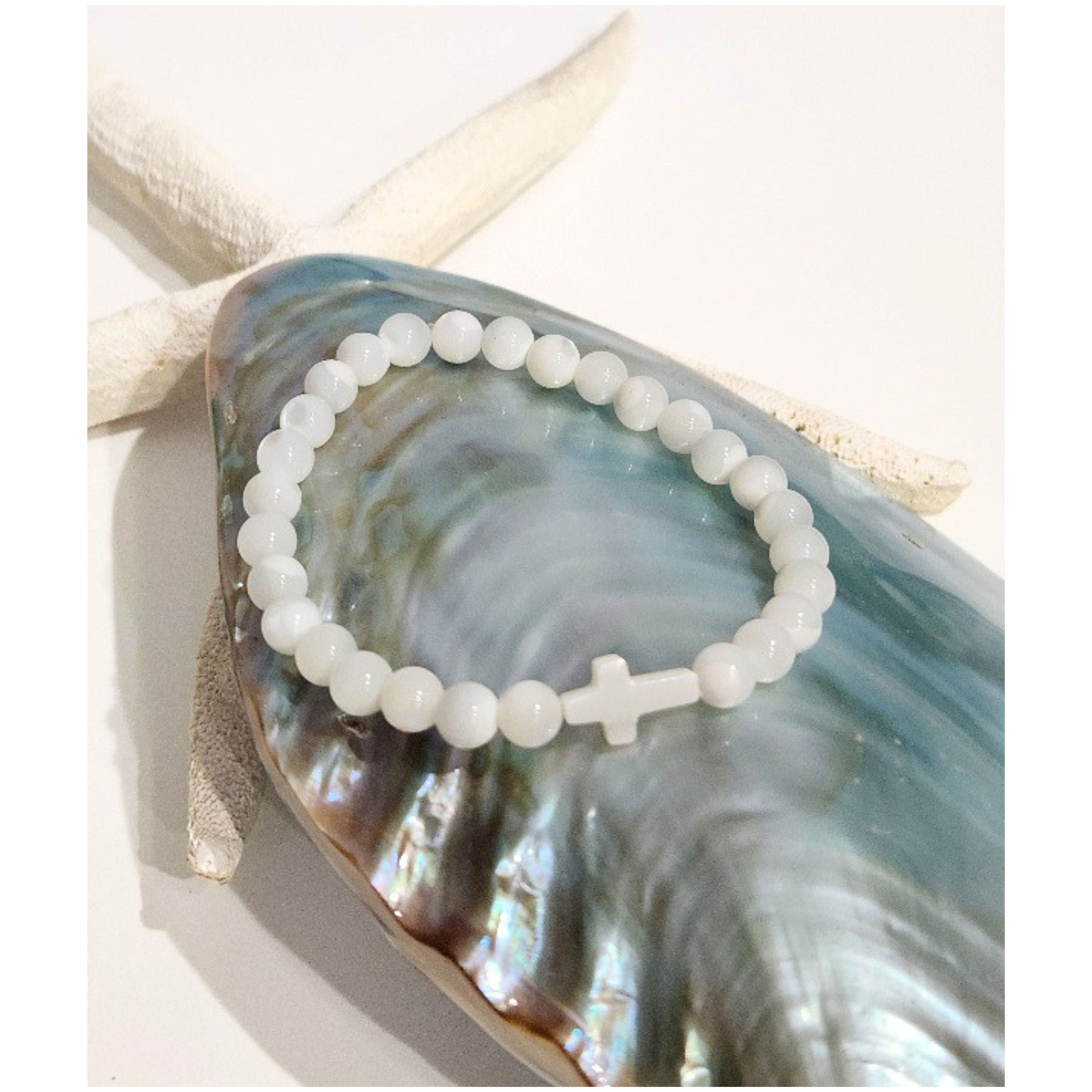 Handmade Mother of Pearl petite cross stretch bracelet displayed on an iridescent blue shell with a decorative starfish accent