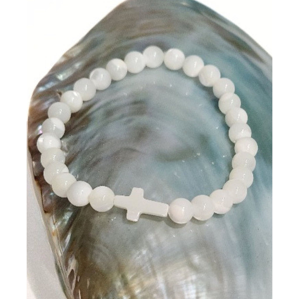 Close up of a Mother of Pearl cross stretch bracelet resting on an iridescent blue shell against a clean white background