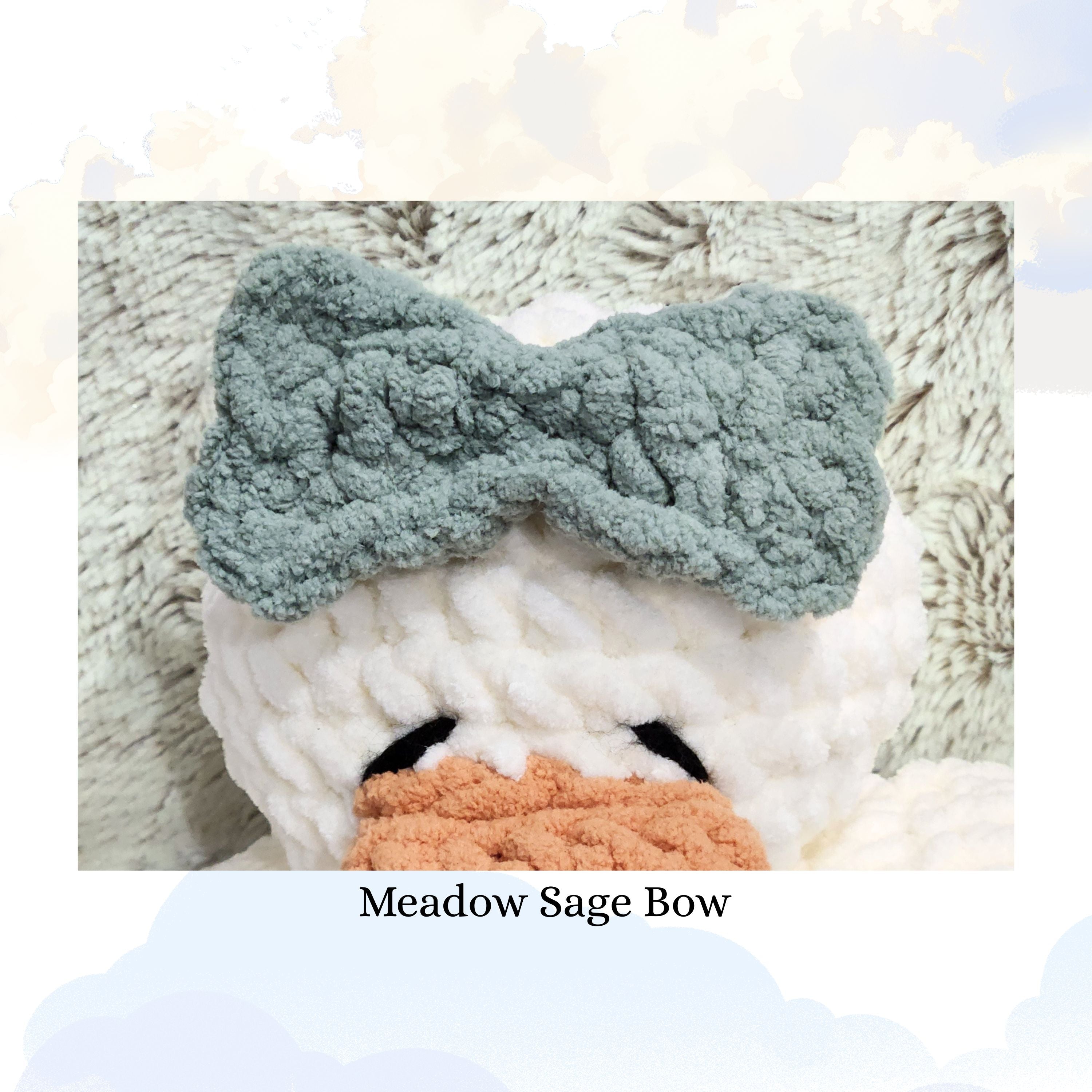 Close up detail of a handmade meadow sage green yarn bow attached to a vanilla cream duck snuggler, highlighting the textured crochet stitch and soft sage color