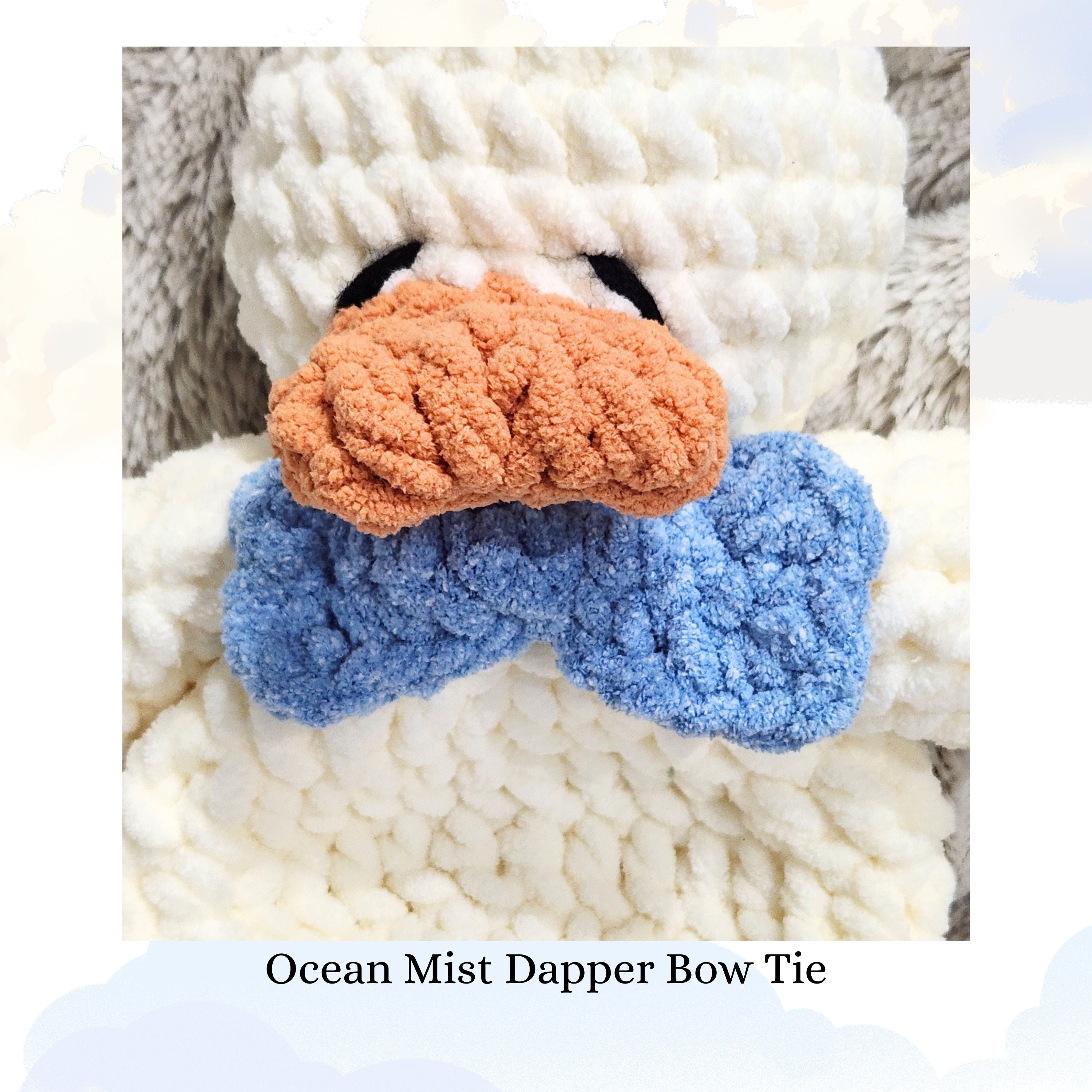 Close up of a Ducky Dreams vanilla cream crochet duck featuring a dapper ocean mist blue bow tie.  The shot highlights the intricate crochet detail, with a plush blanket and whimsical clouds in the soft focus background