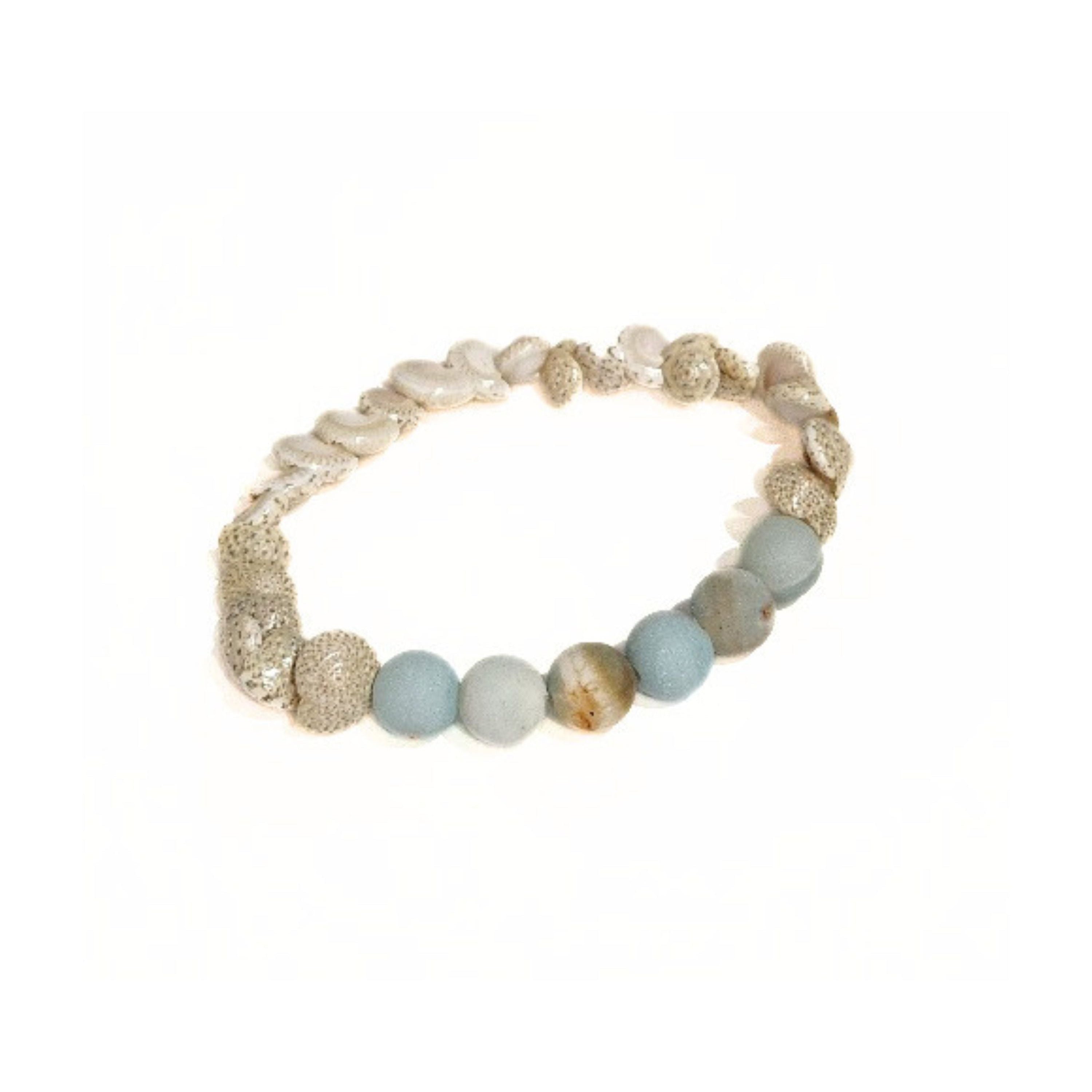A handcrafted Sands of Serenity stretch bracelet by Coastline Boutique, featuring a natural sea spiral shell and six smooth agate beads in sea blue and sand tones, laid in a circle on a clean white background.