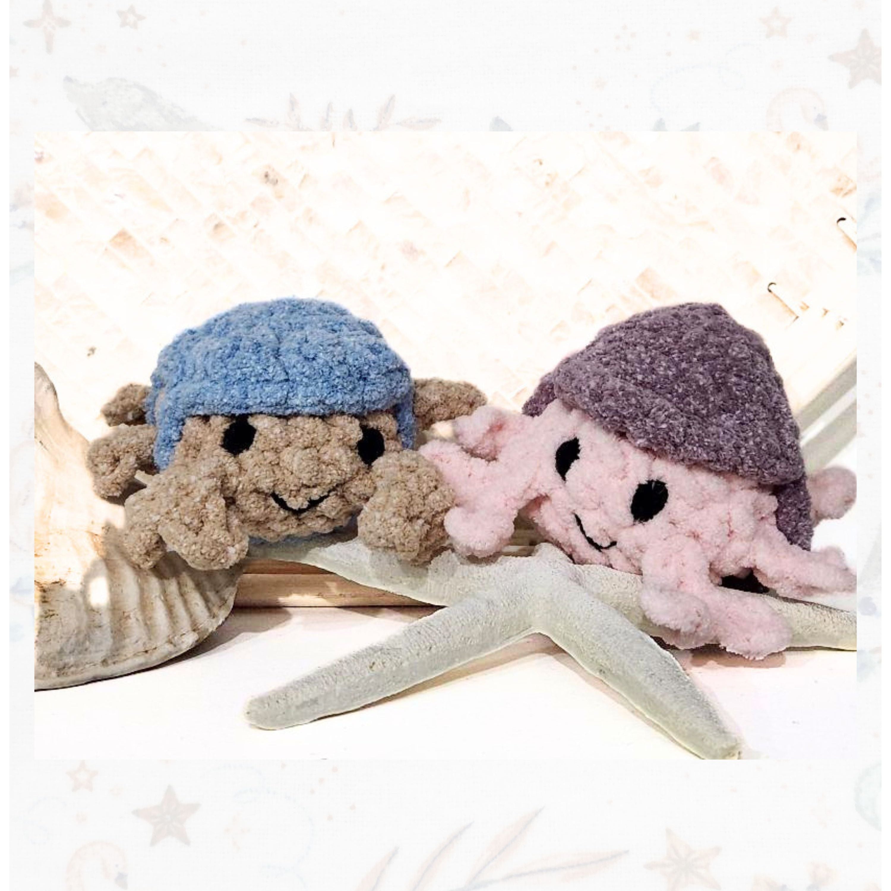 A duo of handmade crochet crabs featuring the sand-toned Shoreline Scout with a blue hat alongside a vibrant pink and purple crab from the Playful Palette collection.