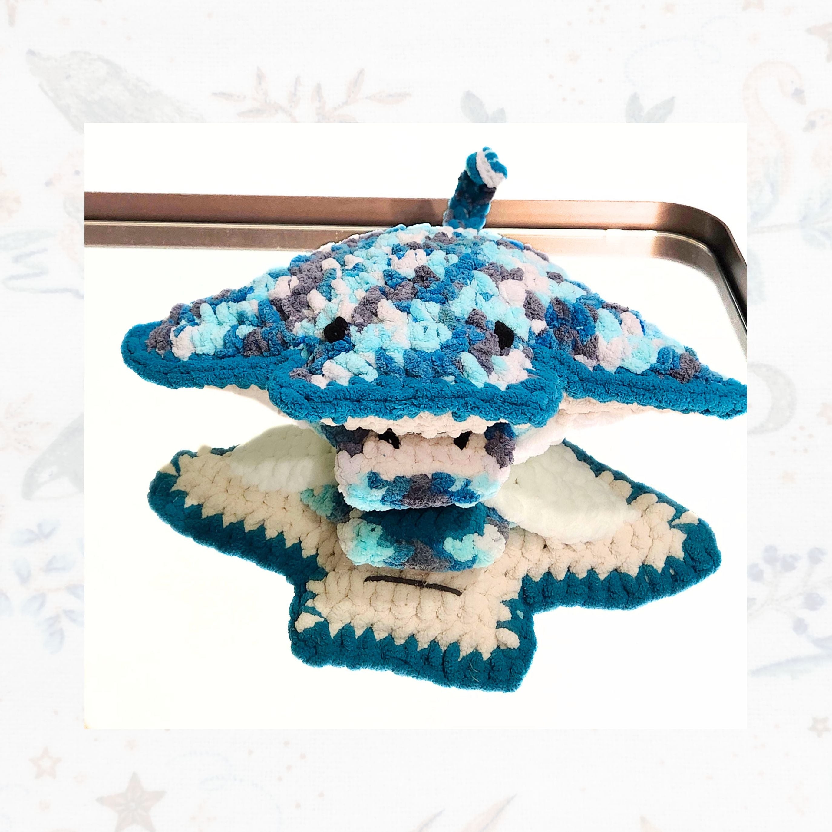 A top-down view of the Seraphina and Sol stingray set resting on a mirror, reflecting the artisan crochet underbelly and mouth detail of the mother while the baby ray stays tucked in her signture pouch, by Coastline Boutique.