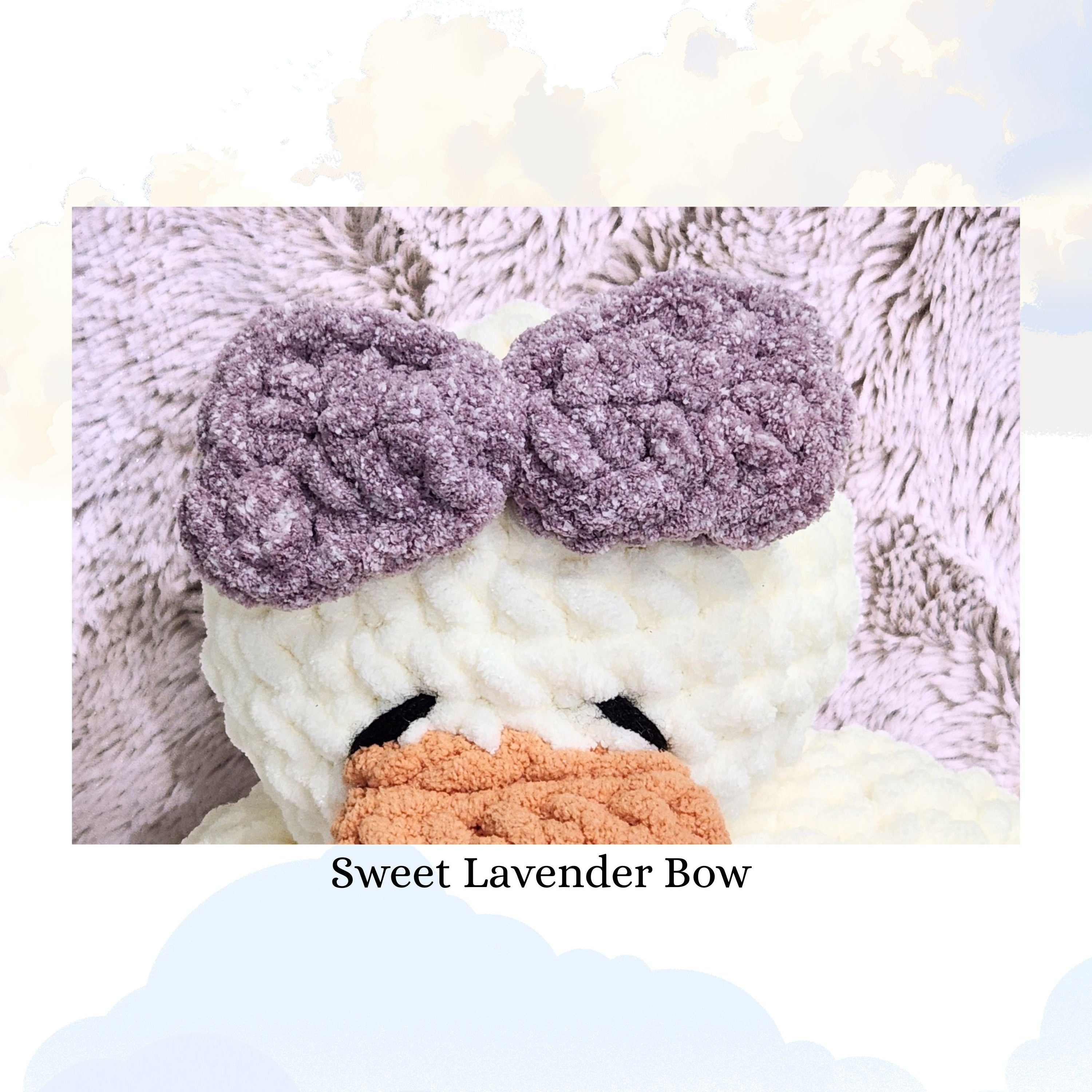 Close up detail of a handmade sweet lavender yarn bow on a vanilla cream duck snuggler, highlighting the soft purple hue and the delicate texture of the crochet stitches