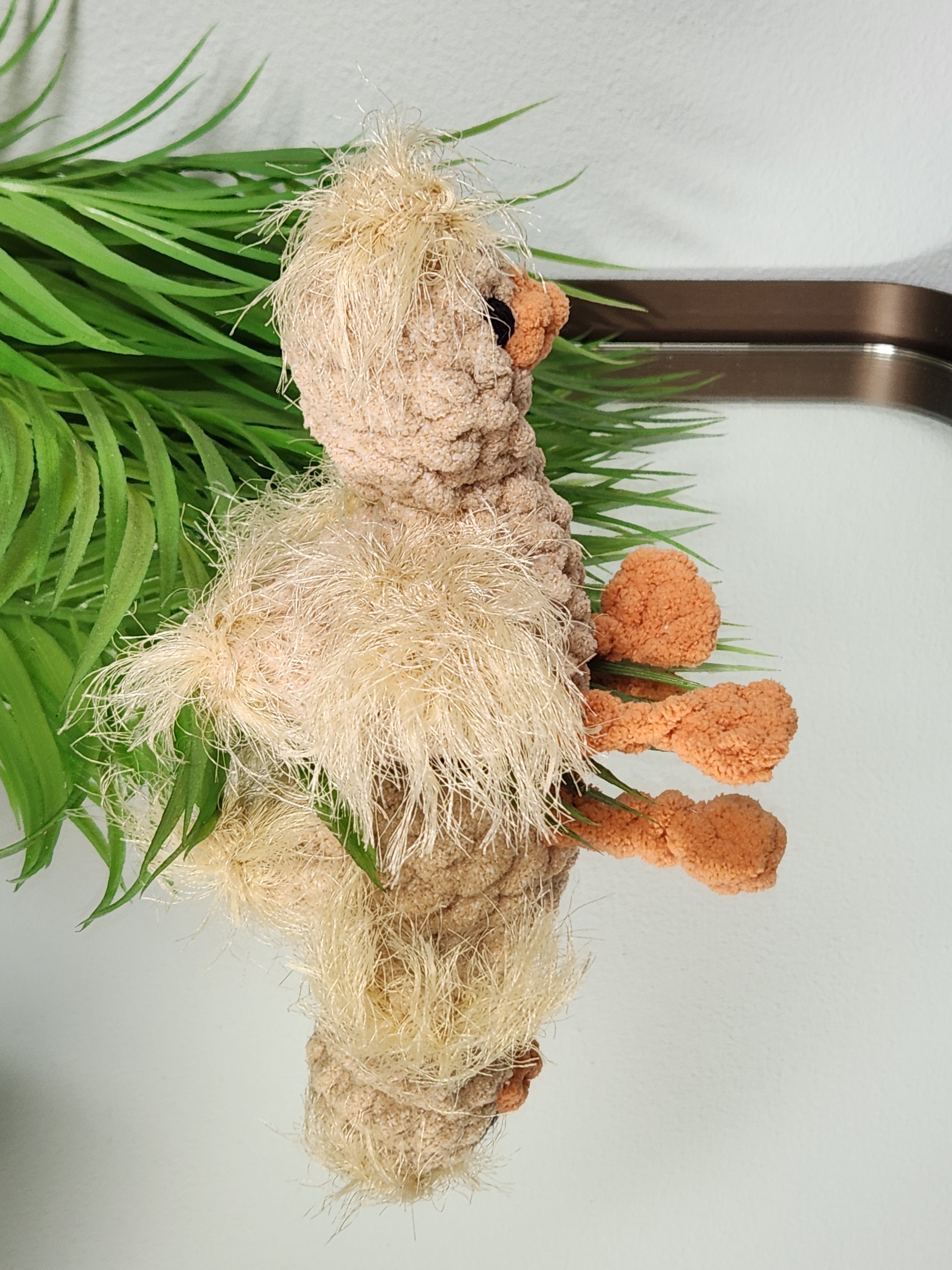 Side profile of Nugget the Gosling on a mirror highlighting the textured fur stitch wings and handcrafted legs in a soft golden yarn