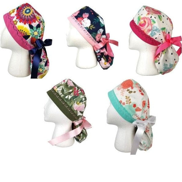 A collection of the Botanical Series ponytail surgical caps by Coastline Boutique featuring varied floral prints in fuchsia, navy, olive, peach, and mango with designer-stitched headbands.