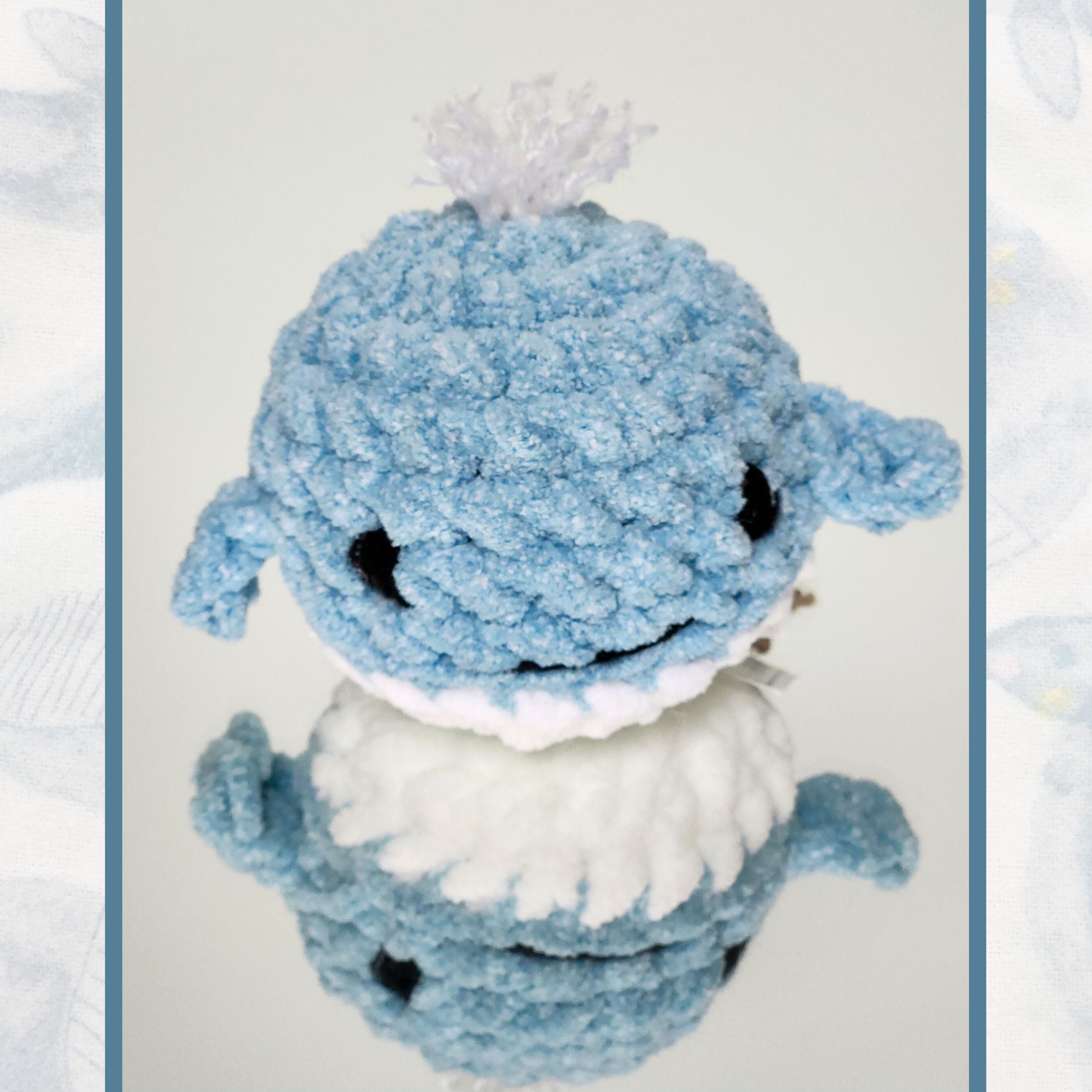 Front view of the Whaley Hello pocket companion, a blue and white crochet splash whale, reflected on a mirror to show the handmade detail of its underside
