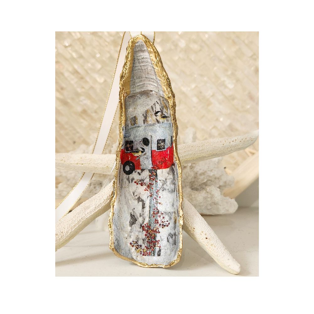 A handcrafted gilded oyster shell ornament featuring a vintage red and silver camper birdhouse design, staged on a coastal background of white coral and a starfish