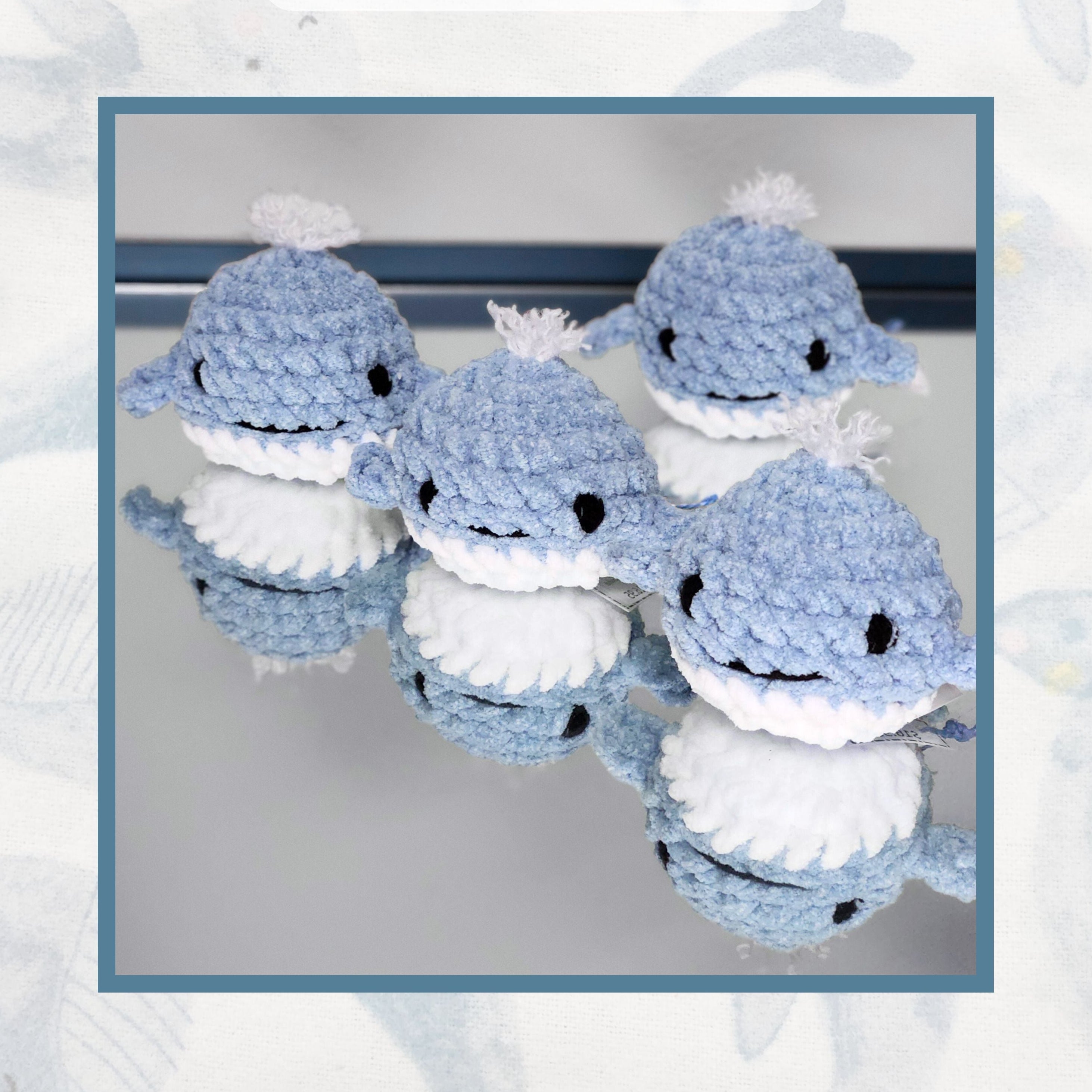 A pod of four Whaley Hello splash whales from the Brejoy Collection, shown on a mirror with soft reflections that showcase their hand stitched craftsmanship.